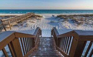 Una escalera de madera que baja a una playa con un paseo de madera y vista al océano.
