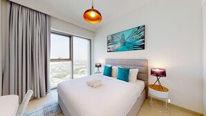 Une chambre d’hôtel avec un grand lit, une vue par la fenêtre, un tableau au mur et une lampe sur une table de chevet.