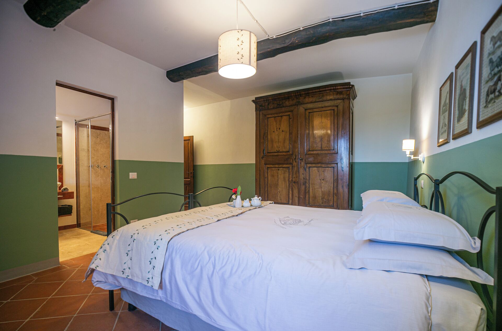 A bedroom with a bed, a wooden wardrobe, a green wall, and a tiled floor.