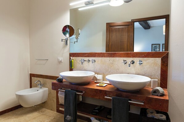A bathroom with two large sinks, a bidet, a mirror, and a towel rack.