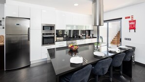 A modern kitchen with white cabinets, stainless steel appliances, a central island with seating, and a staircase leading to another level. - Villa Clara do Sol - Four Bedroom Villa, Sleeps 8 (Estoi)