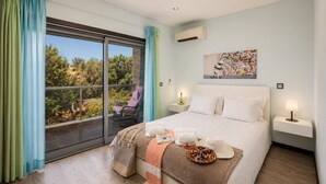 A bedroom with a large bed, a nightstand, a chair, and a view of greenery outside. - Villa Clara do Sol - Four Bedroom Villa, Sleeps 8 (Estoi)