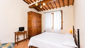 A bedroom with a bed, a wooden wardrobe, a desk with a computer, and a window with curtains.