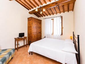 Un dormitorio con una cama, un armario de madera, un escritorio con computadora y una ventana con cortinas.