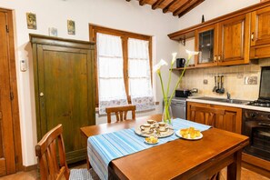 A kitchen with wooden cabinets, a dining table with a blue tablecloth, and a vase with flowers.