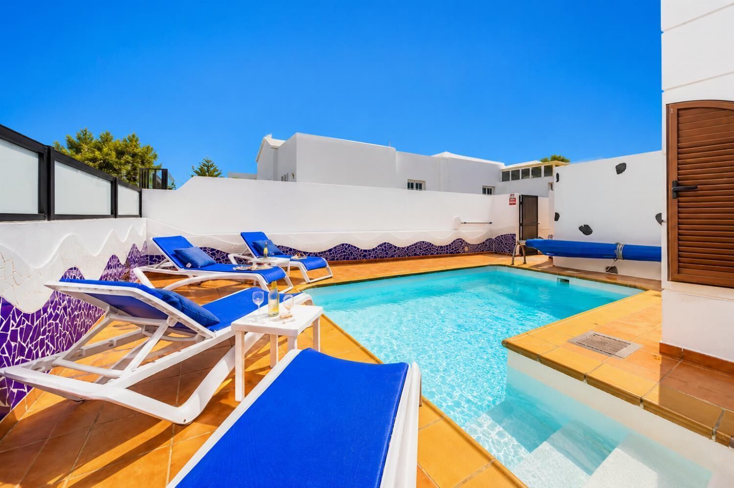 A pool area with lounge chairs, a clear blue pool, and white walls with blue accents.