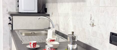 Una cocina con un lavamanos de acero inoxidable, un microondas y una cafetera en la encimera.