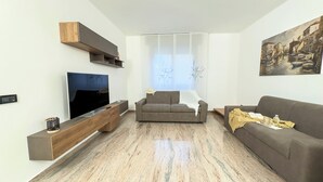 Un salon moderne avec un téléviseur à écran plat, deux canapés, un meuble TV en bois et un tableau accroché au mur.