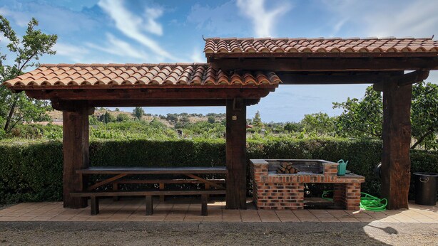 A wooden pergola with a brick barbecue area and a bench.