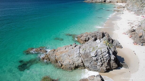 Una playa costera con aguas turquesas cristalinas, formaciones rocosas y una orilla arenosa.