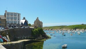 Un pueblo costero con edificios de piedra, un puerto con barcos y un cielo azul despejado.
