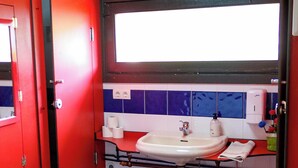 A bathroom with a red door, a sink, and a window above the mirror.