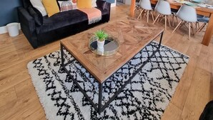 Una sala de estar moderna con un sofá negro, una mesa de centro con una planta y un comedor con una mesa y sillas de madera.