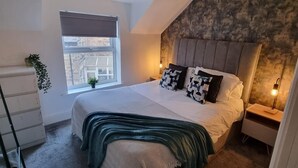 Un dormitorio con una cama grande, tragaluz, vistas al exterior, cómoda y mesita de noche con lámpara.