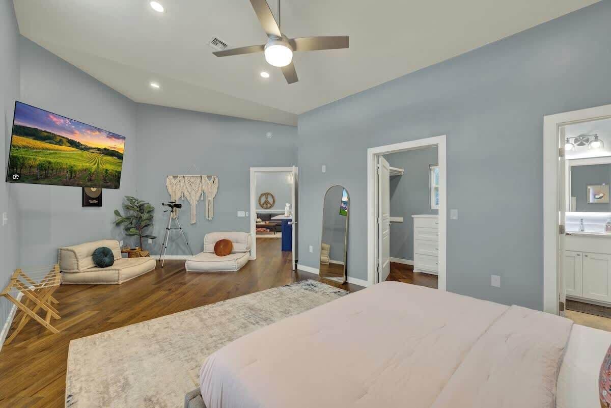Un dormitorio amplio con una cama grande, ventilador de techo, televisor montado en la pared y vista al baño contiguo.
