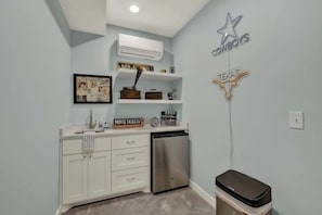 A compact kitchen with white cabinets, a stainless steel refrigerator, and a trash bin.