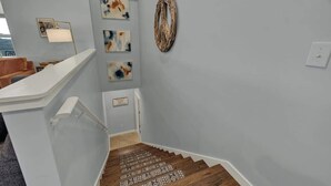 A staircase with a wooden handrail and a wall with abstract art and a woven wall hanging.