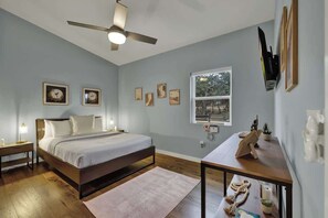 A bedroom with a bed, bedside tables, a ceiling fan, a window, and wall-mounted artwork.