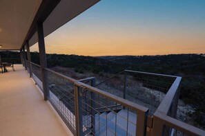 A balcony with a metal railing overlooking a hilly landscape during sunset.