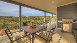 A balcony with a table set for dining, a grill, and a view of a natural landscape.