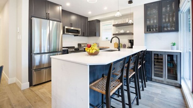 A modern kitchen with stainless steel appliances, a central island with bar stools, and a large window providing natural light.