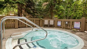 A hot tub surrounded by a wooden fence, with a clock and caution signs visible.