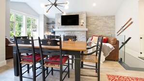 A modern kitchen with a stone wall, a TV mounted above the fireplace, and a dining area with a wooden table and chairs.