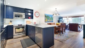 A modern kitchen with dark blue cabinets, stainless steel appliances, and a central island. - Slopeside ski in/out stylish 2BR/2BA HotTub & Pool (Whistler)
