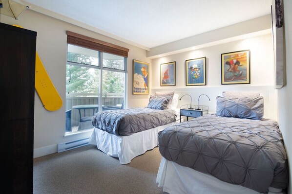 Une chambre avec deux lits, une fenêtre donnant sur un beau paysage et des œuvres d’art encadrées accrochées au mur.