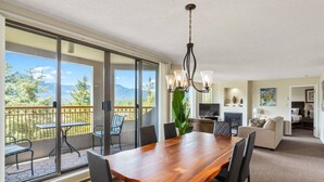 Ampla sala de estar com mesa de jantar de madeira, assentos confortáveis, televisão e varanda com vista panorâmica para as montanhas.