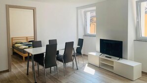 A modern, well-lit room with a bed, a dining table with chairs, a TV on a stand, and a window providing natural light. - 2Curio Court House Charming Lodge (Curio)