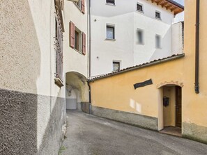 A narrow alleyway with buildings on either side, featuring an archway and a door on the right.