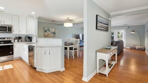 A modern kitchen with white cabinets, a central island, and a dining area with a table and chairs. - Tranquil Villa Golf Course Views in Palmetto Dunes (Hilton Head Island)
