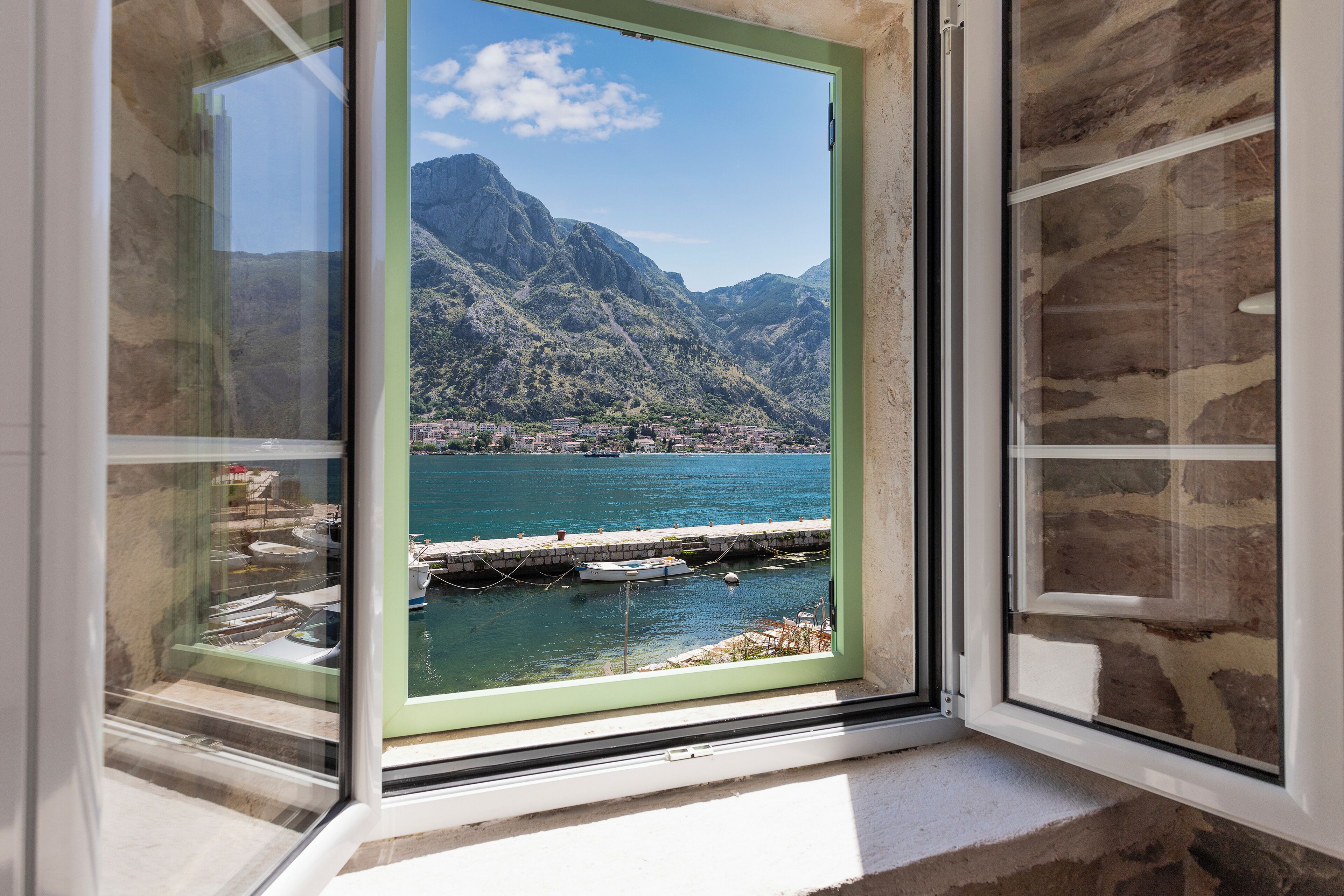 Ein Fenster mit Blick auf einen See, Berge und einen Steg mit Booten.