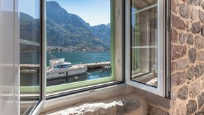 A window with a view of a mountainous landscape, a body of water, and a dock with boats. - Seaside House - 19th century with Free Parking (Kotor)
