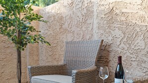 Una silla de mimbre con cojín, una botella de vino y una copa sobre una mesa, con una planta en maceta al lado.