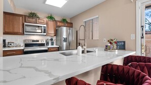 Una cocina moderna con encimera de m ármol, electrodomésticos de acero inoxidable, armarios de madera y una butaca de terciopelo rojo.