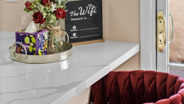 Un área de cocina con una encimera blanca, un florero con flores, una caja de pañuelos y un letrero que dice 'La contraseña del Wifi es...'.