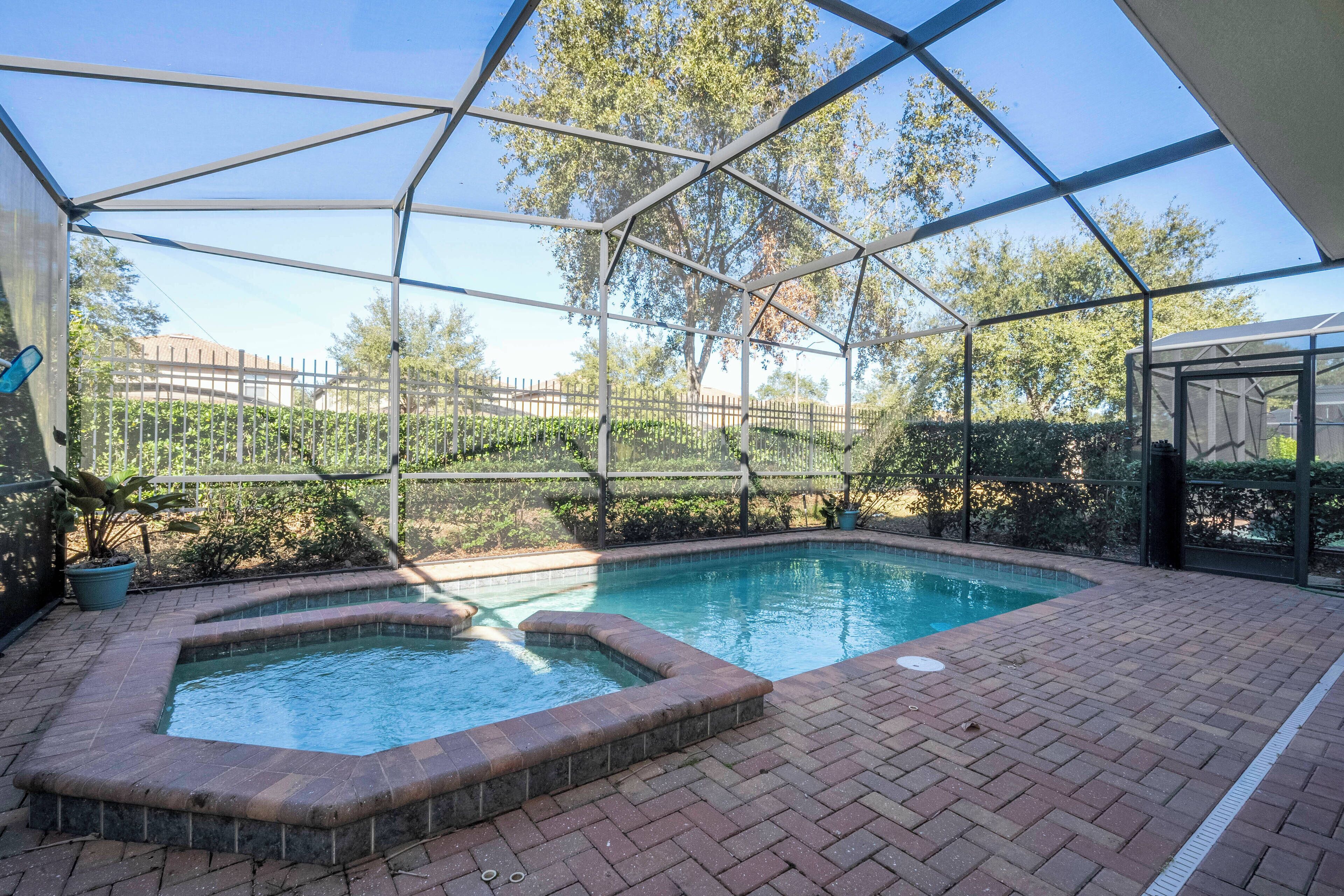 Une piscine entourée d’une enceinte en verre, bordée d’une terrasse en briques et agrémentée de plantes en pot.