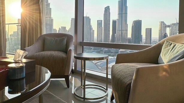 A modern hotel room with a large window offering a view of the city skyline and the Burj Khalifa.