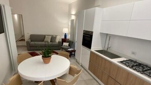 A modern kitchen with white cabinets, a gas stove, and a dining area with a round table and chairs. - BED&BIKEITALA ANGUILLARA SABAZIA AL BORGO - House in the village on the shores of the lake   (ANGUILLARA SABAZIA)