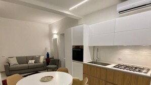 A modern kitchen with white cabinets, a gas stove, and a built-in oven. There is a dining area with a round table and chairs. - BED&BIKEITALA ANGUILLARA SABAZIA AL BORGO - House in the village on the shores of the lake   (ANGUILLARA SABAZIA)
