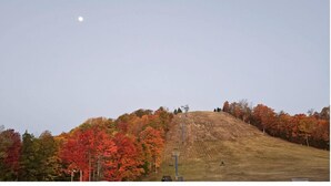 A hill with a ski lift, surrounded by trees with autumn foliage.