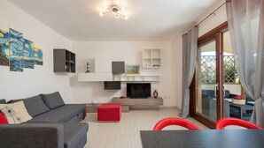 Una sala de estar moderna con un sofá gris, un taburete rojo, televisor de pantalla plana y un comedor con mesa y sillas.