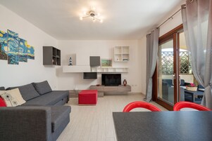 Una sala de estar moderna con un sofá gris, un taburete rojo, televisor de pantalla plana y un comedor con mesa y sillas.