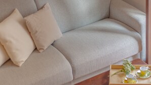 En beige soffa med två kuddar och ett träbricka med en bukett och två koppar på en tillhörande bricka.