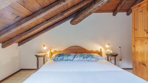 Ett sovrum med ett träpanelat tak, en säng med blommiga kuddar, två sänglampor och en trägarderob.
