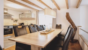 A modern dining area with a wooden table and black chairs, a kitchen in the background, and a unique wooden beam ceiling. - Chalet Naila by we rent (Bruck an der Grossglocknerstrasse)