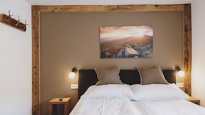A bedroom with a wooden headboard, a bed with white bedding, two bedside lamps, and a painting of a mountain landscape. - Chalet Naila by we rent (Bruck an der Grossglocknerstrasse)