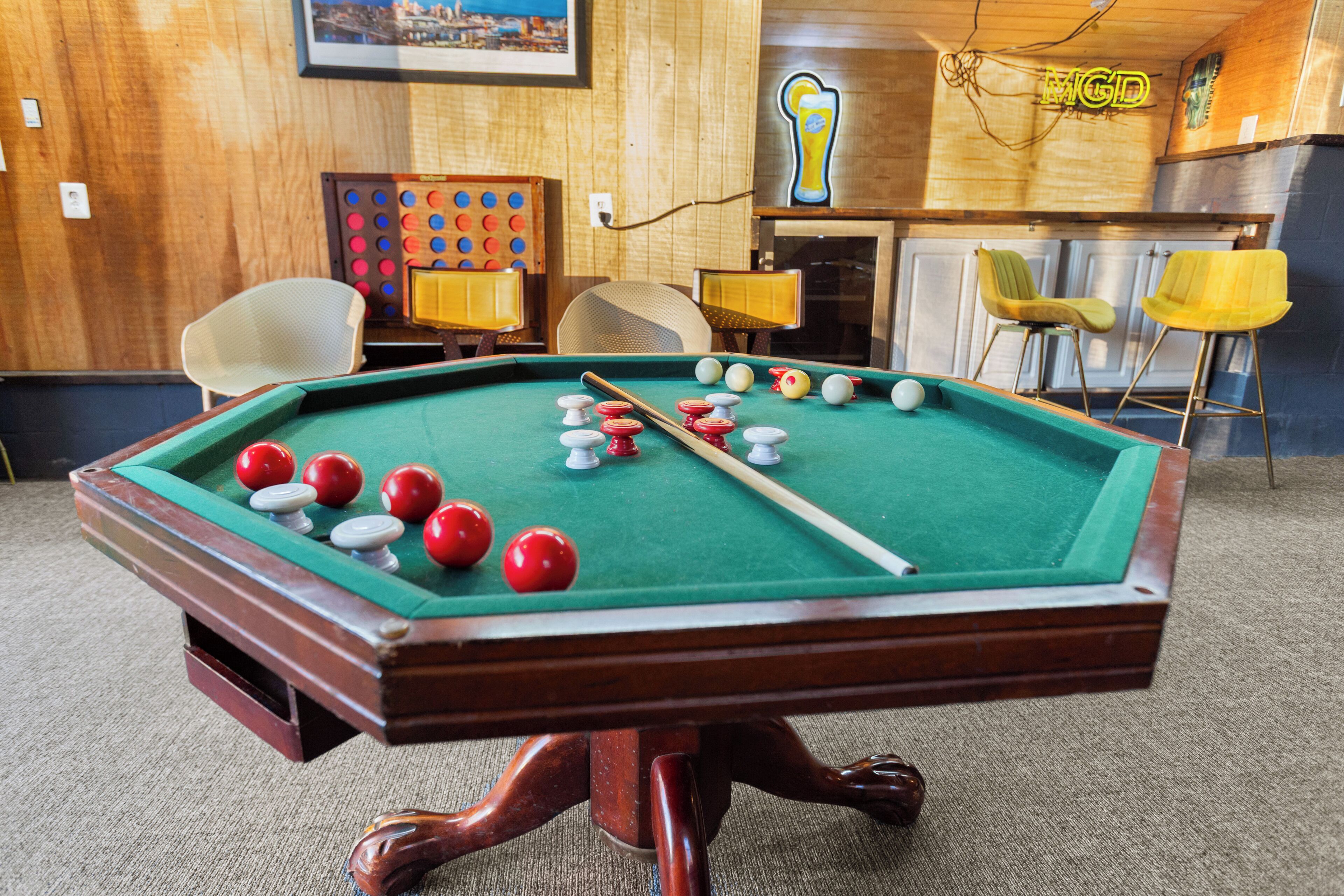 A pool table with balls, chairs, and a neon sign in a room with wooden walls and a carpeted floor.